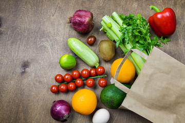 Different food in paper bag on wooden background, close up. Grocery shopping concept, top view