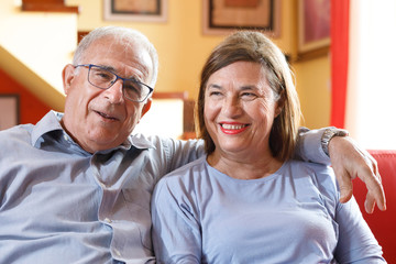 coppia di anziani si abbraccia felice e sorride nel divano del salotto  di casa
