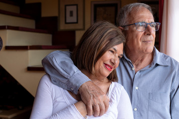 coppia di anziani si abbraccia felice e sorride in piedi nel salotto di casa