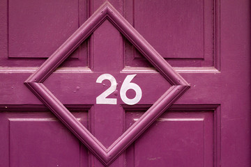 House number 26 on a purple wooden front door in a crooked picture frame
