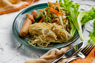 Salad of fresh vegetables on a plate with leaves, next to toasted pasta spaghetti with egg and meat sausage, a Hearty lunch, everyday productsfor a home dinner