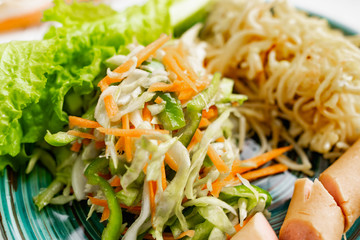 Salad of fresh vegetables on a plate with leaves, next to toasted pasta spaghetti with egg and meat sausage, a Hearty lunch, everyday productsfor a home dinner