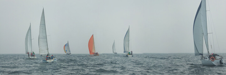 Yacht regatta at sea during the rain and orange sail in a foggy morning floats on the sea. Wide panorama