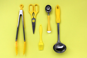 kitchen ladle accessories, scissors, tongs, brush, yellow ice cream spoon on a yellow background
