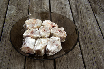 Pieces of fresh raw fish lie on a white plate. The fish is collapsed in flour. The plate is standing on a wooden table.
