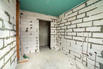Interior of an apartment room with bare walls and ceiling under construction.