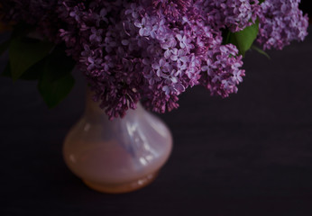 Still life with a bouquet of lilacs and compote of berries. A glass of compote, a jug, a bouquet, a book and glasses on a dark wooden table. Still life near the window.
