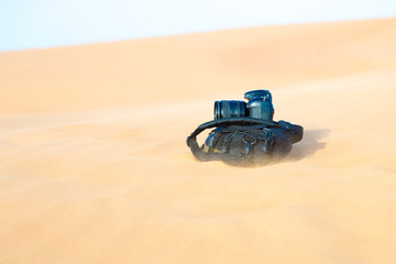 The camera lies on a backpack in the desert. Photographer's bag lies on the hot sand during a...