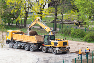 excavator collects sand into a truck, builders are watching