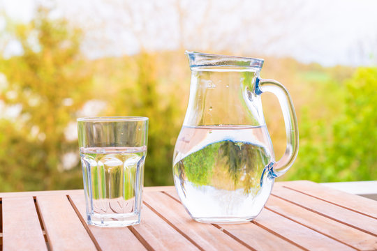 jug with water and a glass on a wooden table on the nature in the garden