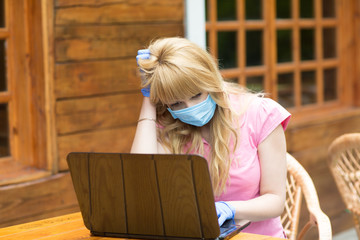 beautiful girl works at a remote work with a computer in a mask and gloves