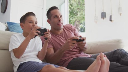 Hispanic father and son sitting on floor at home playing video game and giving each other high five - shot in slow motion - Powered by Adobe