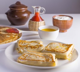 Blinis with filling on a plate , red berry sauce, sour cream in a bowl, melted butter