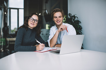 Dreamy creative female employee looking away smiling while his male colleague using laptop computer for research,teen hipsters learning together in online business school satisfied with education