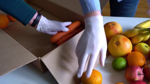 Volunteers in protective medical gloves putting fruits and vegetables In donation box.