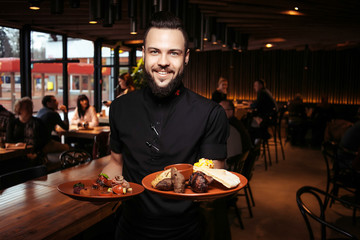 Cheerful bearded waiter with kebab and salad in a georgian restaurant. A discerning waiter in black clothes, with a beard and a portion of kebabs