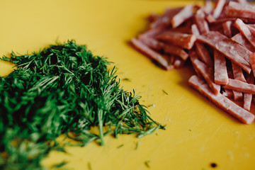 ham sausage with lard with white dots sliced ​​in strips on a yellow plate blackboard background and green dill