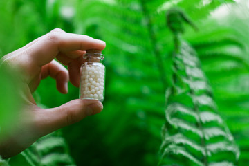 Man holding Bottles of homeopathic globules on green fern background. Homeopathy medicine.