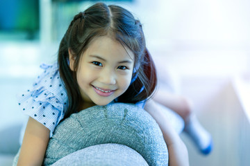 Young asian kid is lying on sofa backrest in living room with smiling face and happiness, playing with parent during weekend. Cheerful daughter staying at home with social distancing and school close