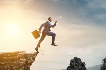 Black businessman jumping over mountain stones