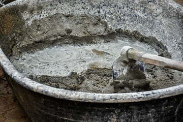A worker mixing cement mixture with a hoe for house maintenance foundation base plastery work in a large mixing bowl