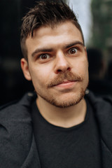 Portrait of a young man walking around the city. Brunette, beard. Cheerful, beautiful smile.