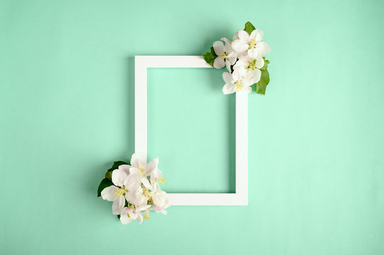 Beautiful white flowers and photo frame on a green background. Top view, copy space.