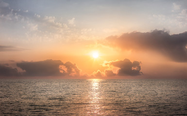 Obraz na płótnie Canvas Sunset at sea. The sun is hiding behind the clouds.