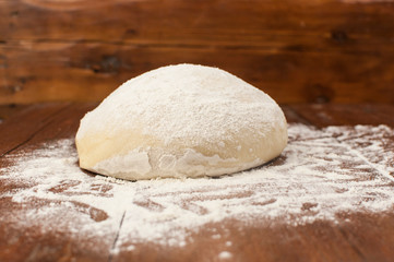 Fototapeta na wymiar Ball of pizza dough on a rustic wooden background with dusting of flour