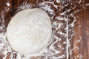 Ball of pizza dough on a rustic wooden background with dusting of flour
