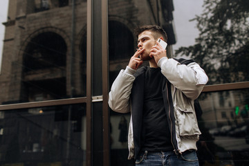 Portrait of happy young man walking on the street and looking aside while talking by his phone.