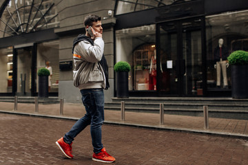 Portrait of happy young man walking on the street and looking aside while talking by his phone.