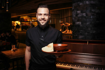 Cheerful bearded waiter with rich tomato soup with beef, rice. A discerning waiter in black clothes, with a beard and a tomato soup