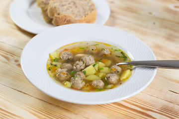 Bowl of meatball soup with spoon and bread on wooden table