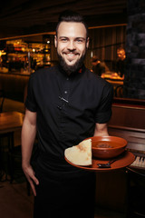 Cheerful bearded waiter with rich tomato soup with beef, rice. A discerning waiter in black clothes, with a beard and a tomato soup