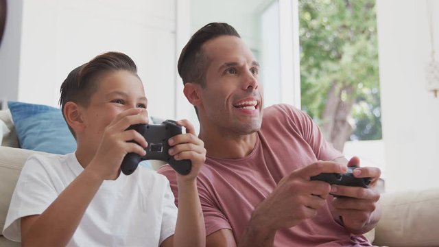 Hispanic father and son sitting on floor at home playing video game and giving each other high five - shot in slow motion