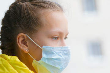 Portrait of a girl near the window in a medical mask during isolation.