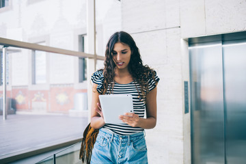 Millennial female in casual wear using digital tablet for blogging and share multimedia files via...