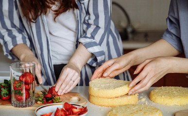Women make a cake: cut strawberries into fillings and prepare layers of sponge cake. Hands in the frame. Homemade cake with berry filling. Series