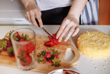 Woman is cutting thin slices of strawberries for the filling of the cake. Female hands in the frame. Homemade cake. Birthday cake. Series