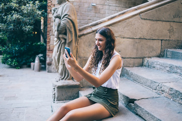 Fototapeta na wymiar Cheerful young woman taking selfie outside old building