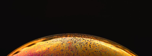 Rainbow soap bubble on black background. Strange colorful planet. 