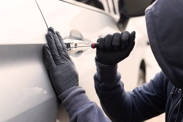 Close up car thief hand holding screwdriver tamper yank and glove black stealing automobile trying door handle to see if vehicle is unlocked  trying to break into inside. 