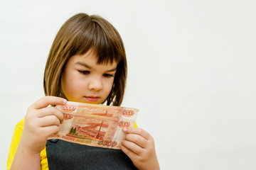a girl of 8 years of Asian appearance holds in her hands banknotes of 5 thousand Russian rubles on...