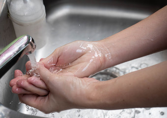 Closeup woman washing hands under the water tap in the kitchen.  Hygiene concept...