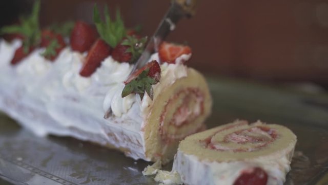 Hands of unrecognizable woman cutting freshly baked sweet strawberry Long-Cake Roll, also called Strawberry roulade