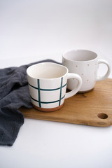 New clay cups for hot drinks stand on a cutting wooden board next to a blue kitchen towel on a light isolated background. Kitchenware with an elegant look.
