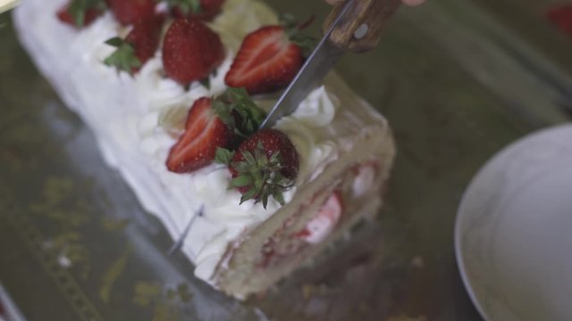 Hands of unrecognizable woman cutting freshly baked sweet strawberry Long-Cake Roll, also called Strawberry roulade