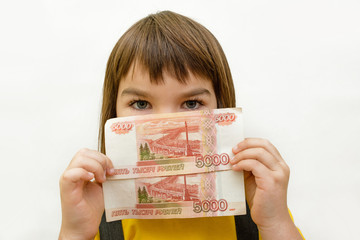 a girl of 8 years of Asian appearance holds in her hands banknotes of 5 thousand Russian rubles on...
