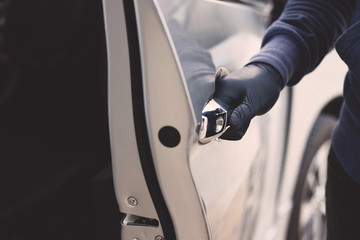 Close up hand pulling the handle of a car thief  wearing black clothes and glove stealing automobile trying door handle to see if vehicle is unlocked  trying to break into. 